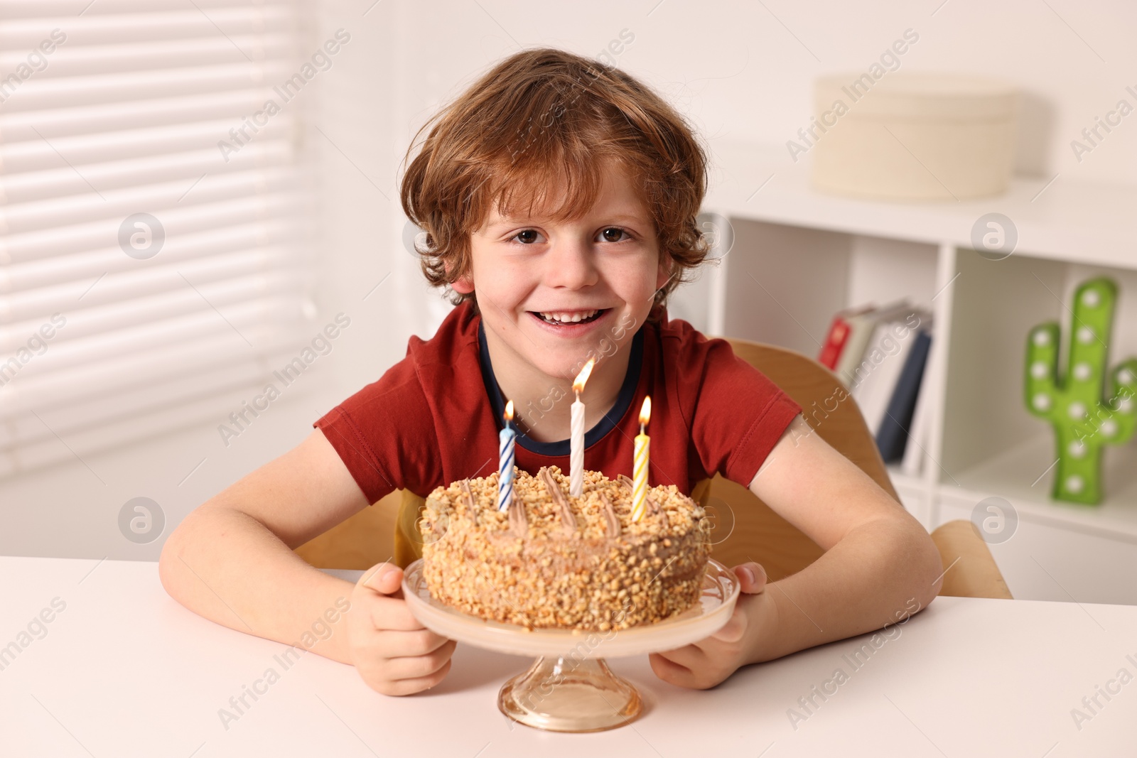 Photo of Cute boy with birthday cake at table indoors