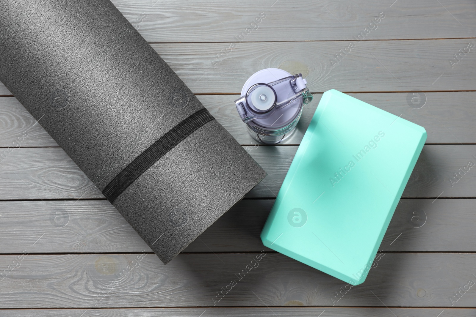 Photo of Exercise mat, yoga block and bottle of water on grey wooden floor, flat lay
