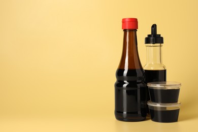 Bottles and bowls with soy sauce on yellow background, space for text