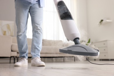 Photo of Man cleaning floor with steam mop at home, closeup