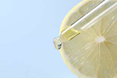 Dripping cosmetic serum from pipette onto lemon slice against light blue background, closeup. Space for text