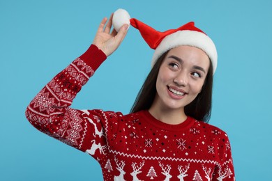 Happy young woman in Christmas sweater and Santa hat on light blue background