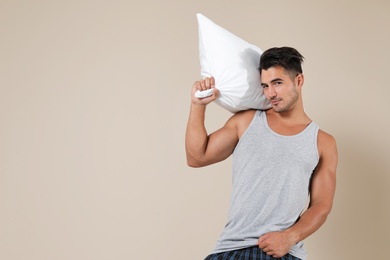 Young man with soft pillow on color background