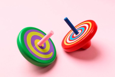 Photo of Two colorful spinning tops on pink background, closeup