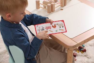 Photo of Little boy playing with set of wooden animals and fence at table indoors. Child's toy