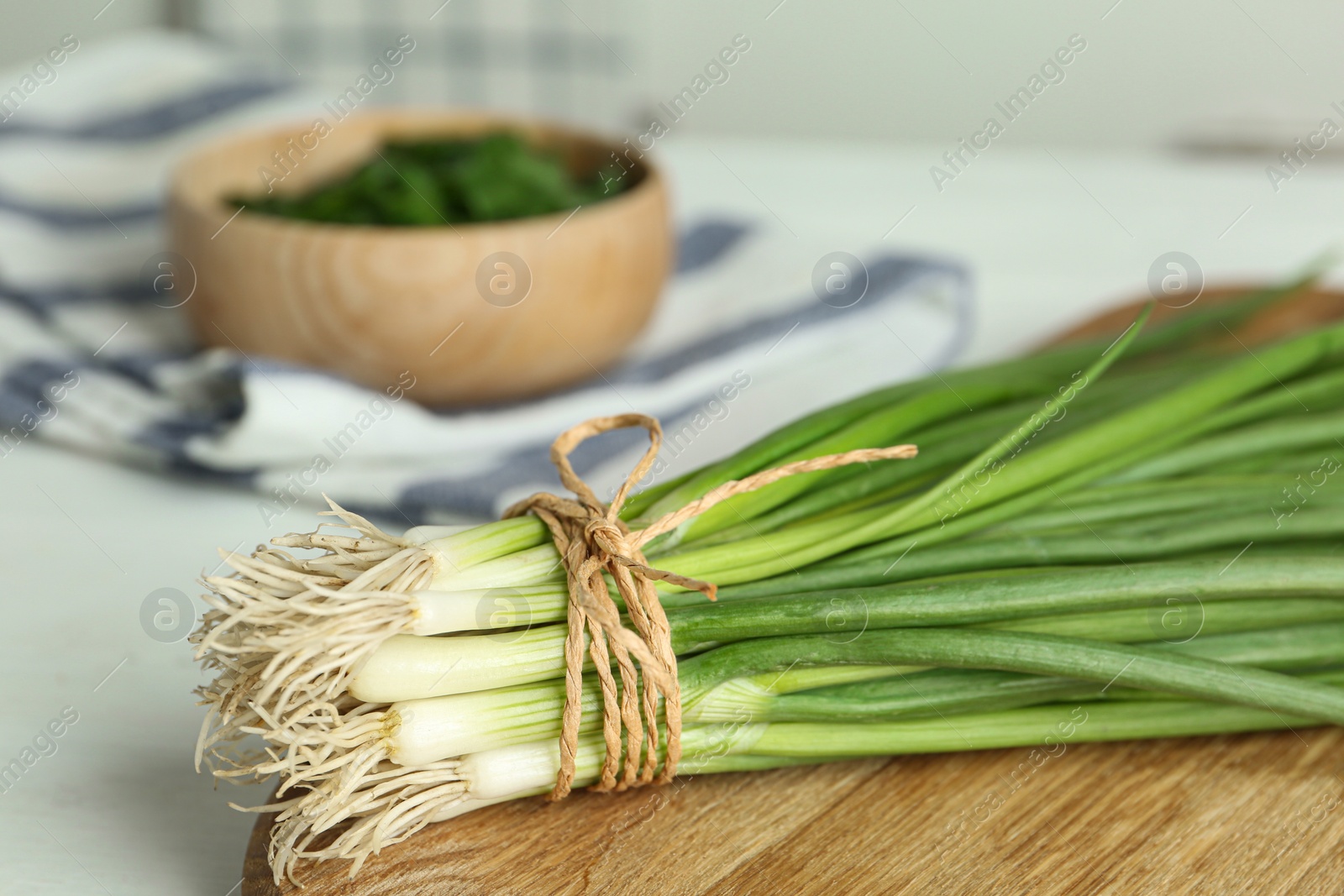 Photo of Fresh green spring onions on wooden board, closeup