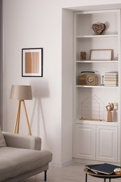 Stylish shelves with different decor elements and lamp in room. Interior design
