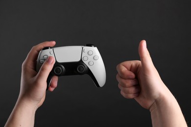 Photo of Woman using wireless game controller and showing thumbs up on dark background, closeup