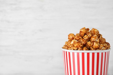 Photo of Paper cup with caramel popcorn on light background. Space for text