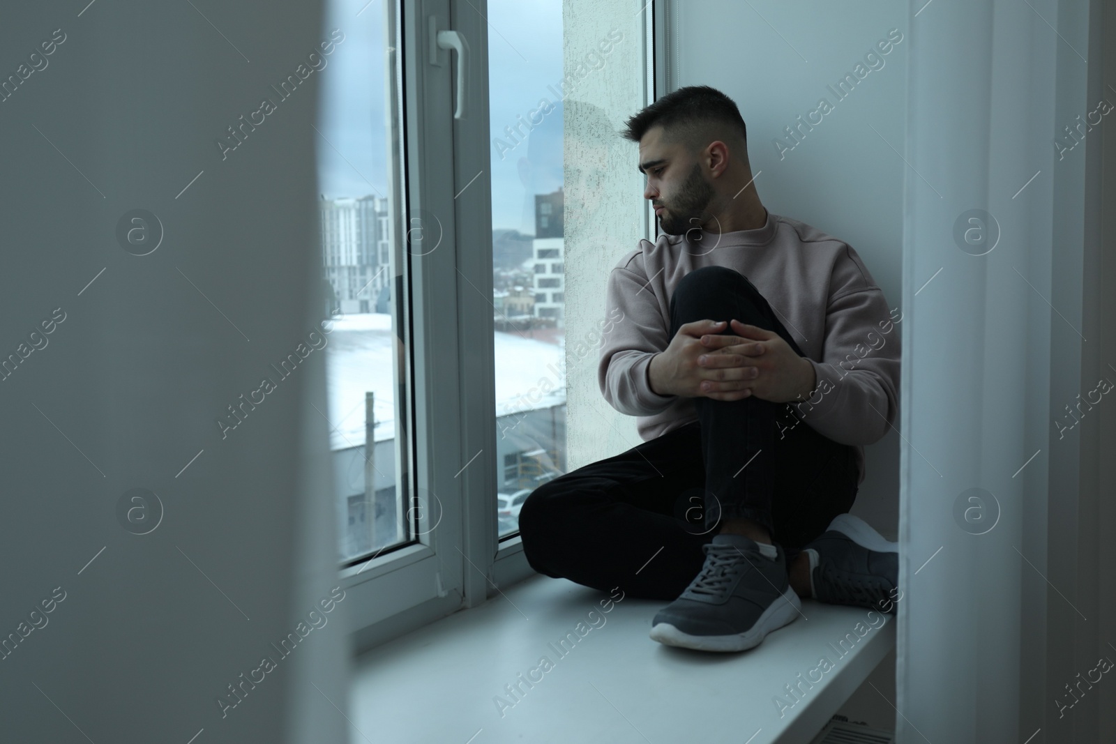 Photo of Sad man sitting on sill and looking at window indoors