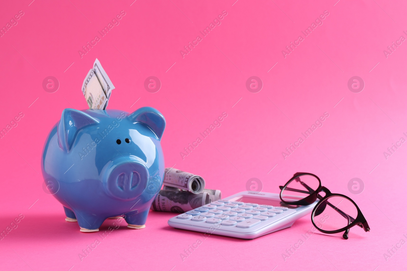 Photo of Financial savings. Piggy bank, dollar banknotes, glasses and calculator on pink background