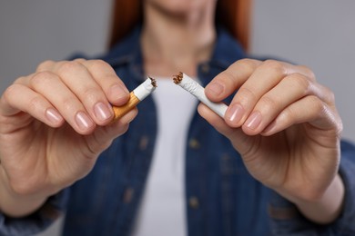 Photo of Stop smoking concept. Woman holding pieces of broken cigarette on light gray background, closeup