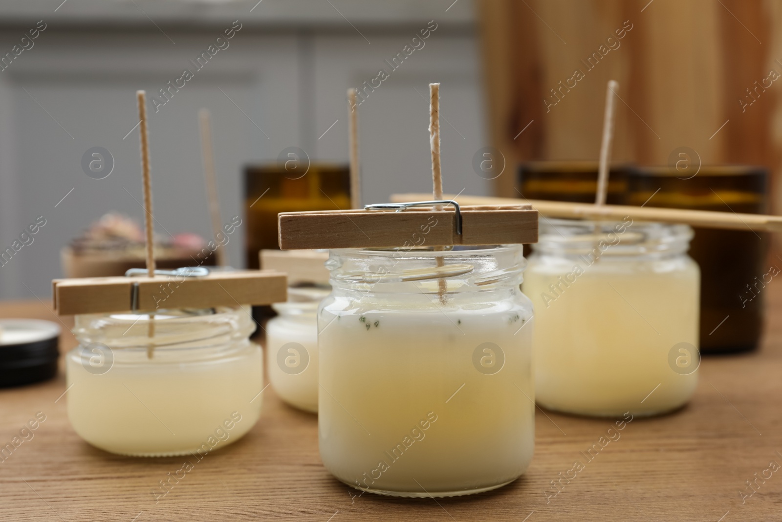 Photo of Glass jars with wax on wooden table indoors. Handmade candles