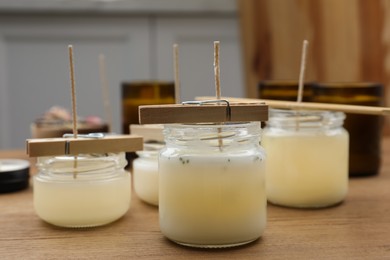 Glass jars with wax on wooden table indoors. Handmade candles