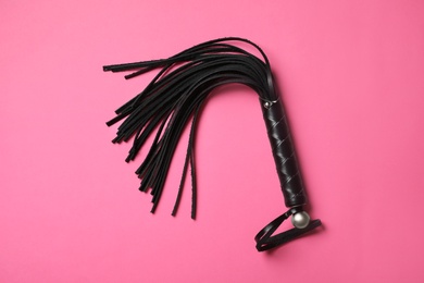 Photo of Black whip on pink background, top view. Accessory for sexual role play