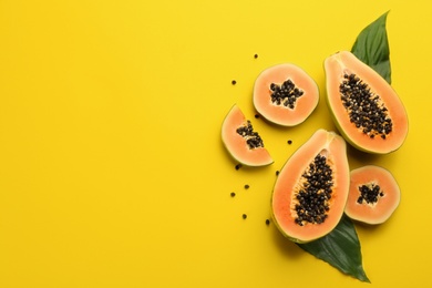 Photo of Fresh ripe papaya fruits with green leaves on yellow background, flat lay. Space for text