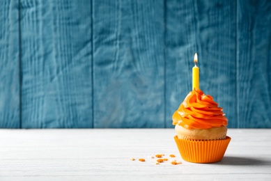 Photo of Delicious birthday cupcake with burning candle on table