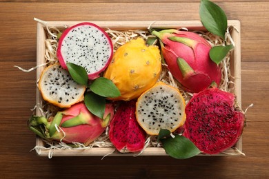 Photo of Delicious cut and whole dragon fruits in crate on wooden table, top view