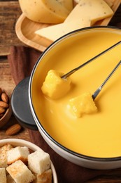 Pot of tasty cheese fondue and forks with bread pieces on table, above view