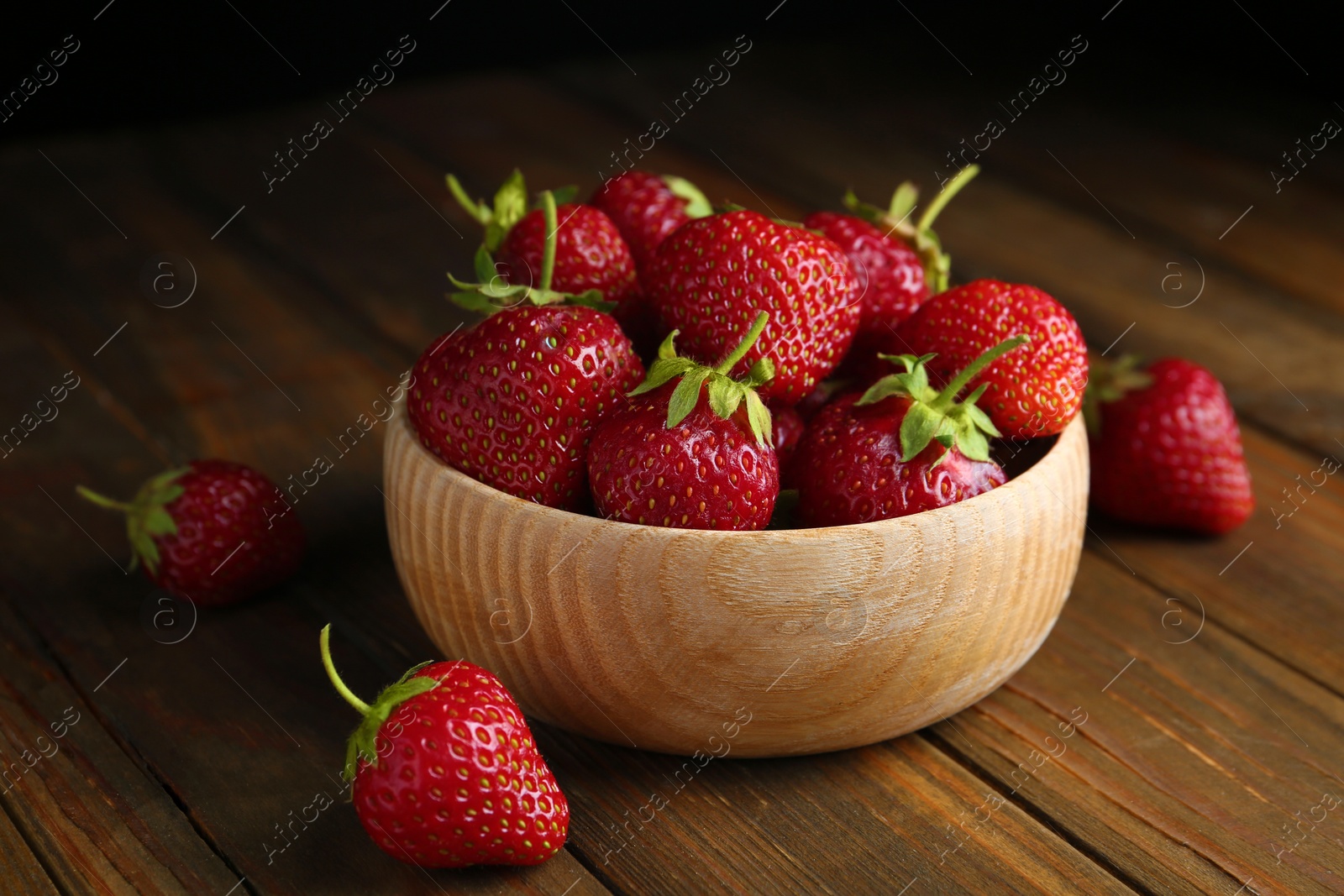 Photo of Delicious ripe strawberries in bowl on wooden table