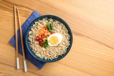 Photo of Bowl of noodles with broth, egg, vegetables and chopsticks served on wooden table, flat lay. Space for text