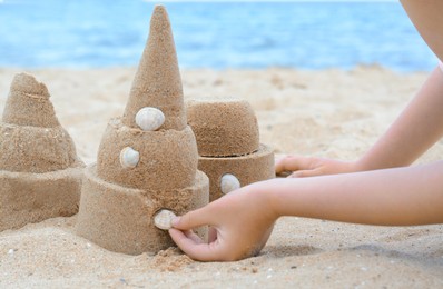 Photo of Child decorating sand castle with shell on beach, closeup