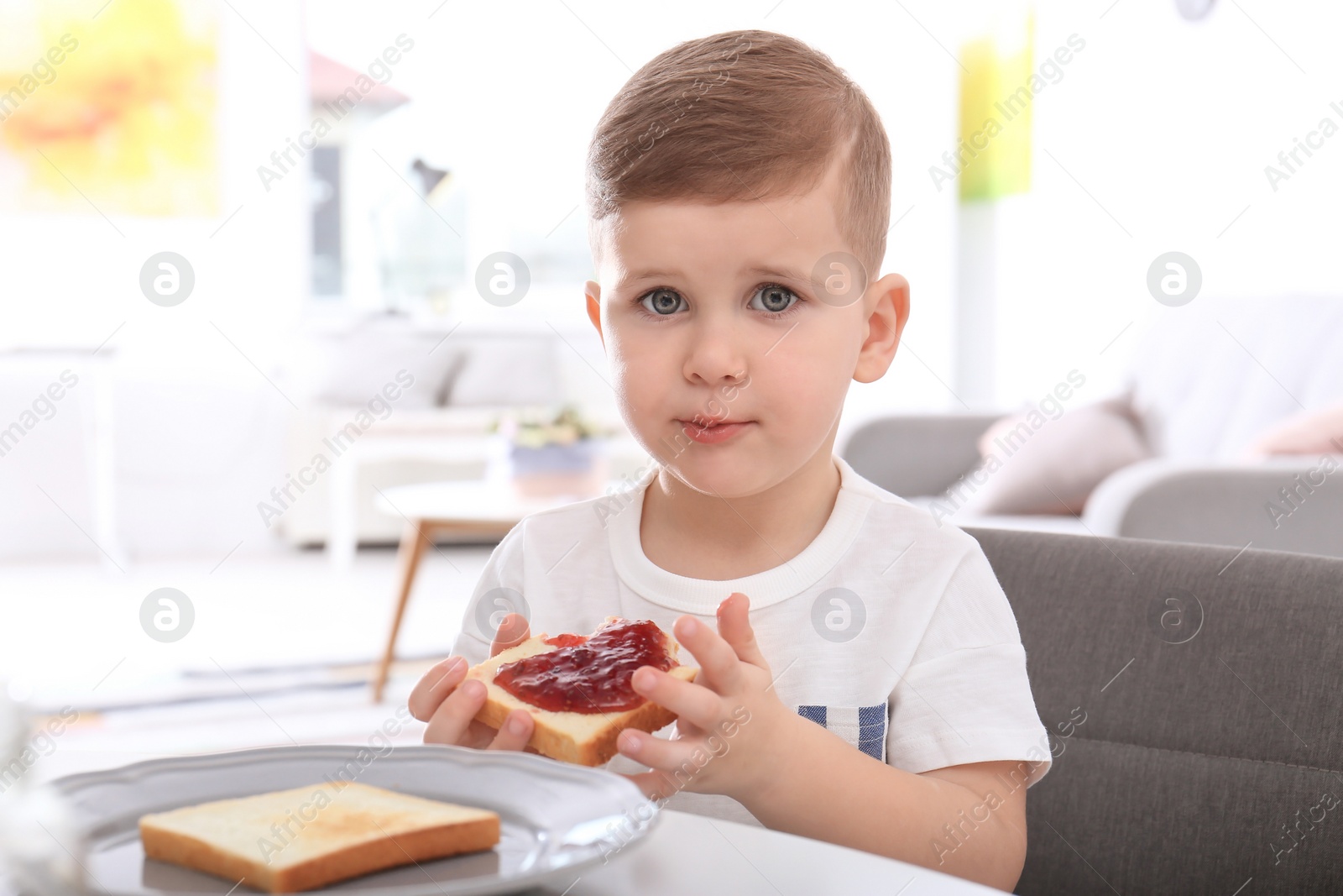 Photo of Cute little boy eating toast with sweet jam at table