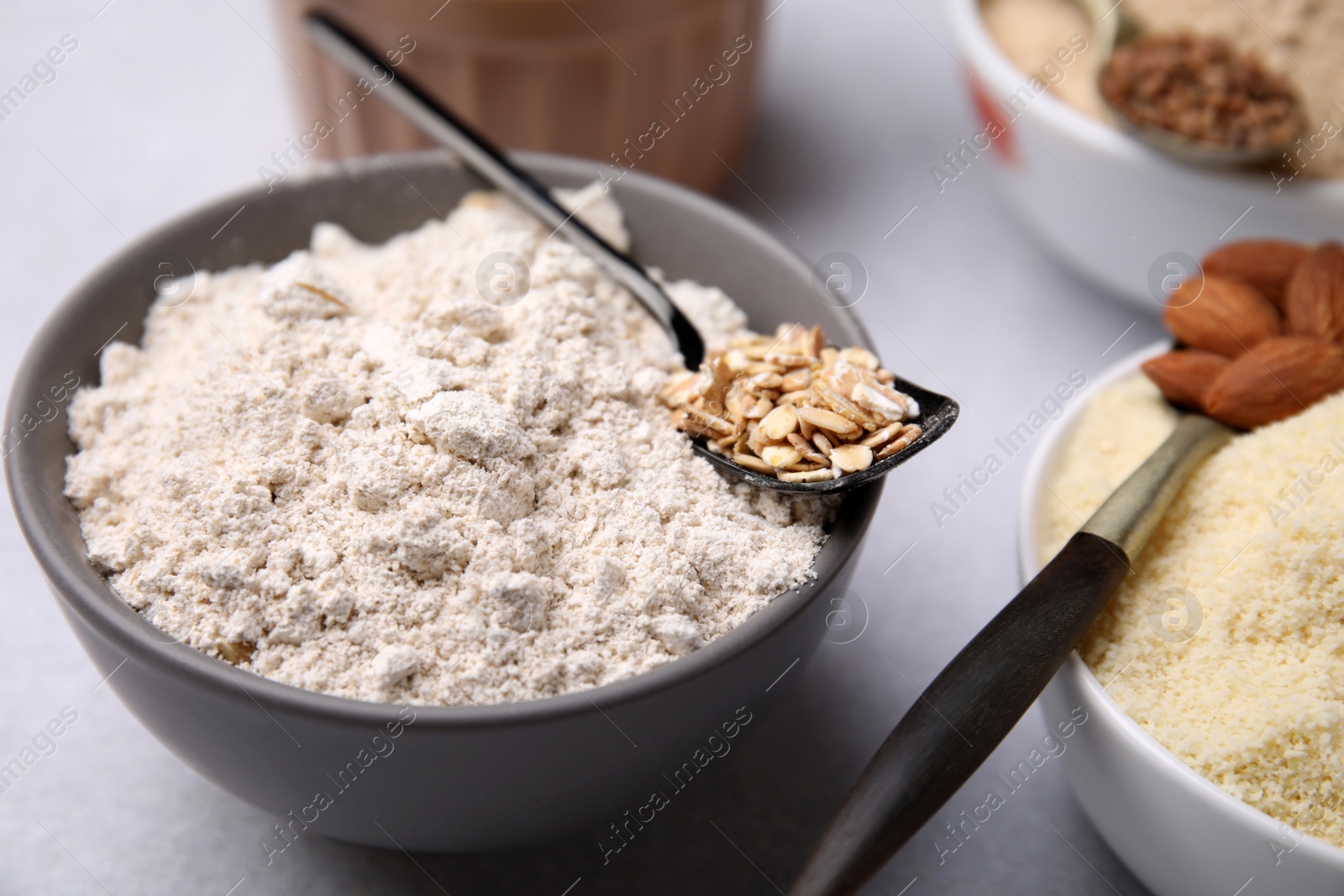 Photo of Bowls with different types of flour and ingredients on light grey table, closeup