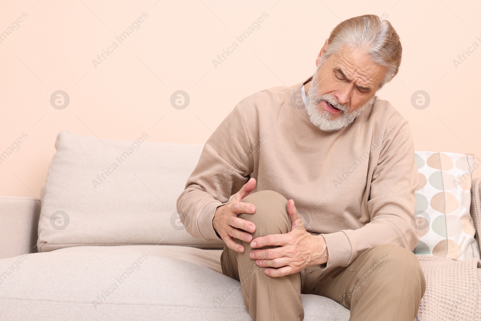 Photo of Senior man suffering from pain in his knee at home, space for text. Arthritis symptoms