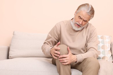 Senior man suffering from pain in his knee at home, space for text. Arthritis symptoms