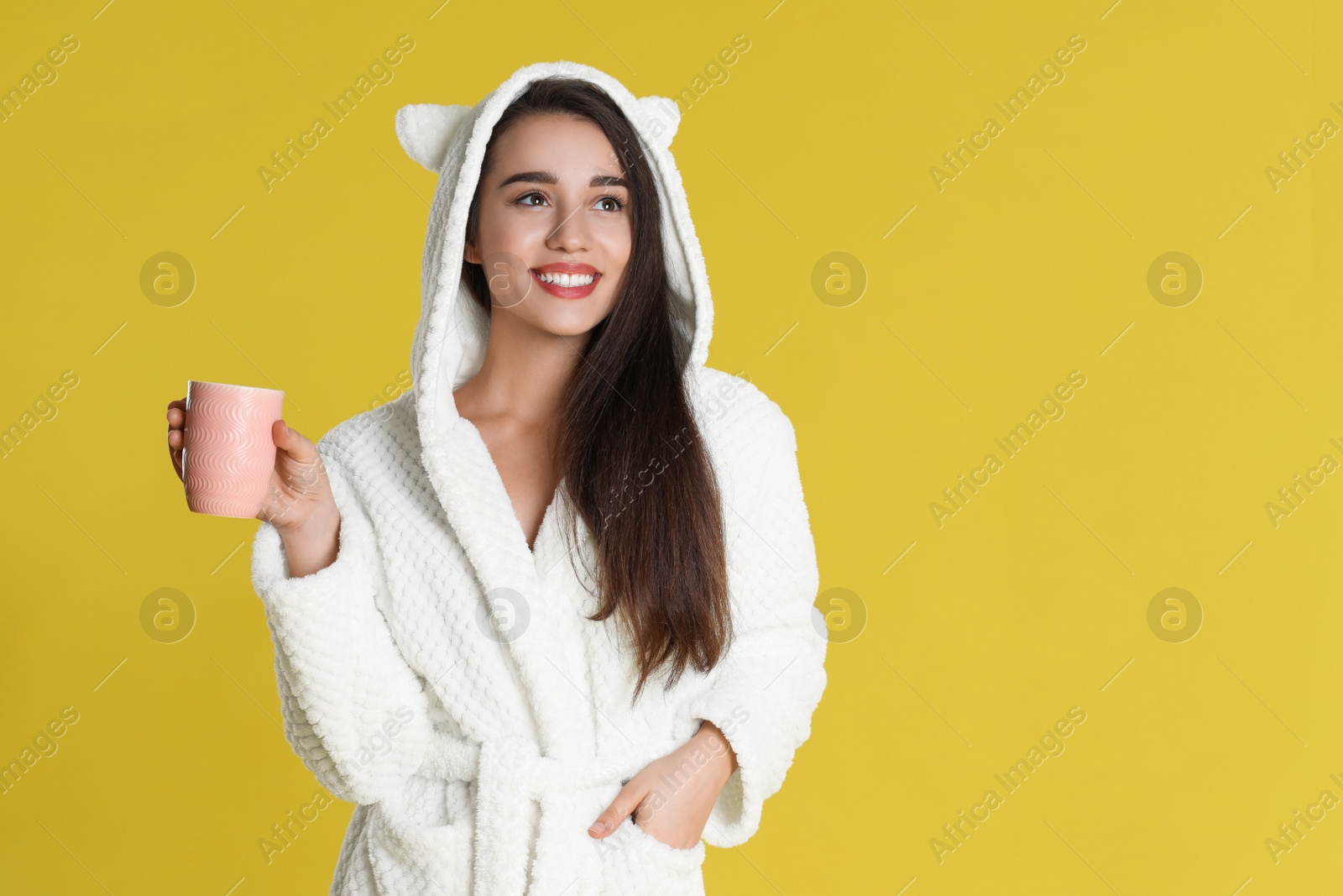 Photo of Young woman in bathrobe with cup of morning drink on yellow background. Space for text
