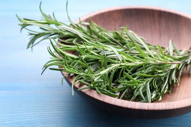 Photo of Sprigs of fresh rosemary in bowl on light blue wooden table, closeup