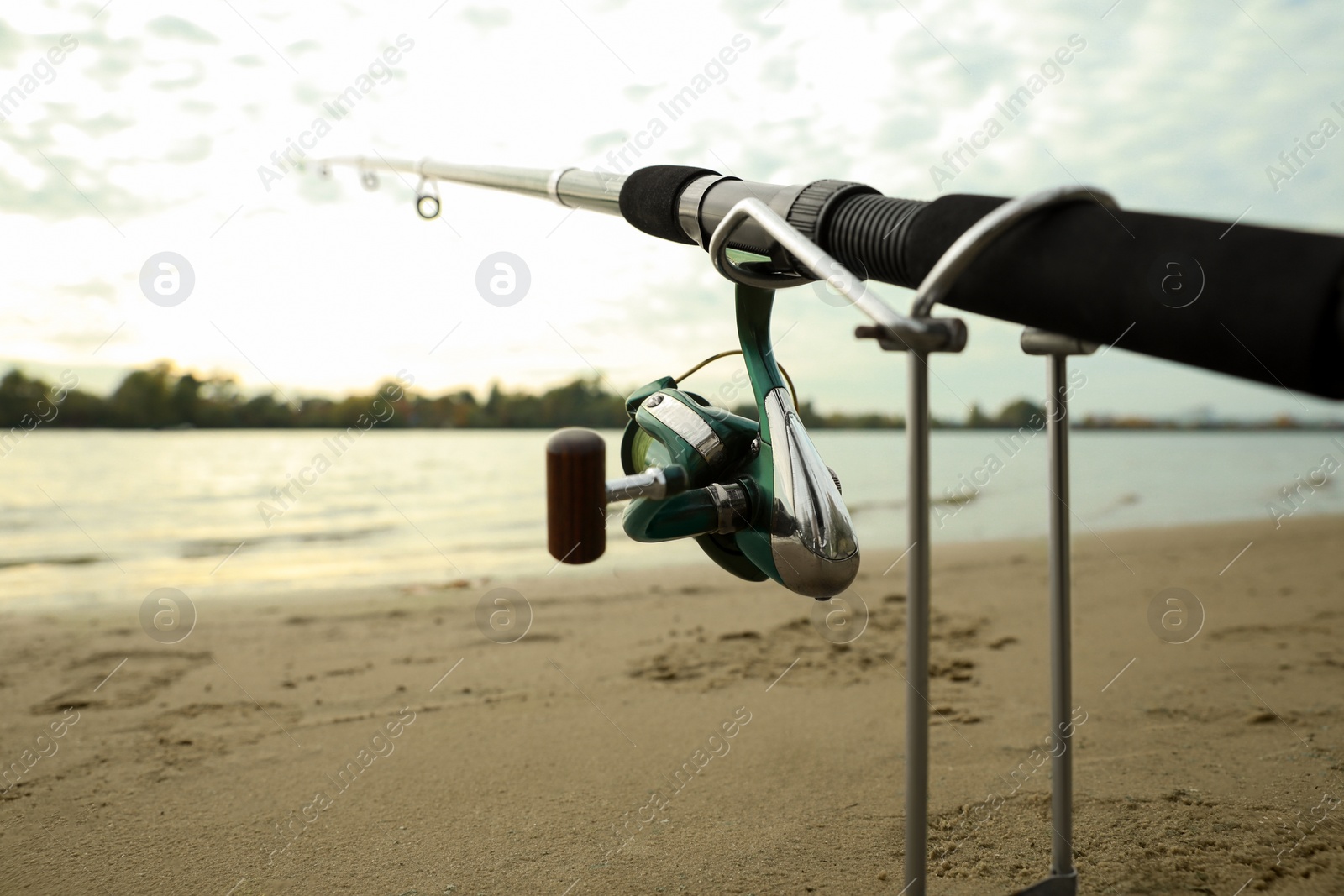 Photo of Fishing rod with reel on sand near river, closeup. Space for text