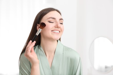 Photo of Beautiful young woman applying makeup with brush at home