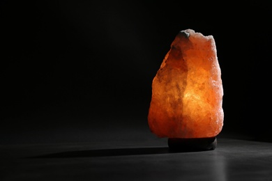 Photo of Himalayan salt lamp on table against black background. Space for text