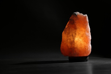 Himalayan salt lamp on table against black background. Space for text