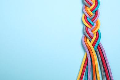Photo of Top view of braided colorful ropes on light blue background, space for text. Unity concept
