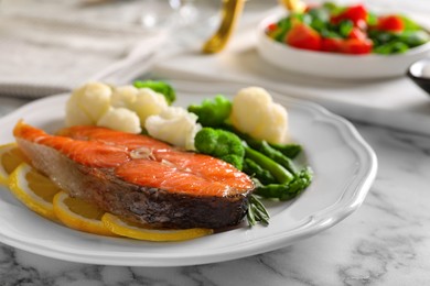 Photo of Healthy meal. Tasty grilled salmon with vegetables and lemon served on white marble table, closeup