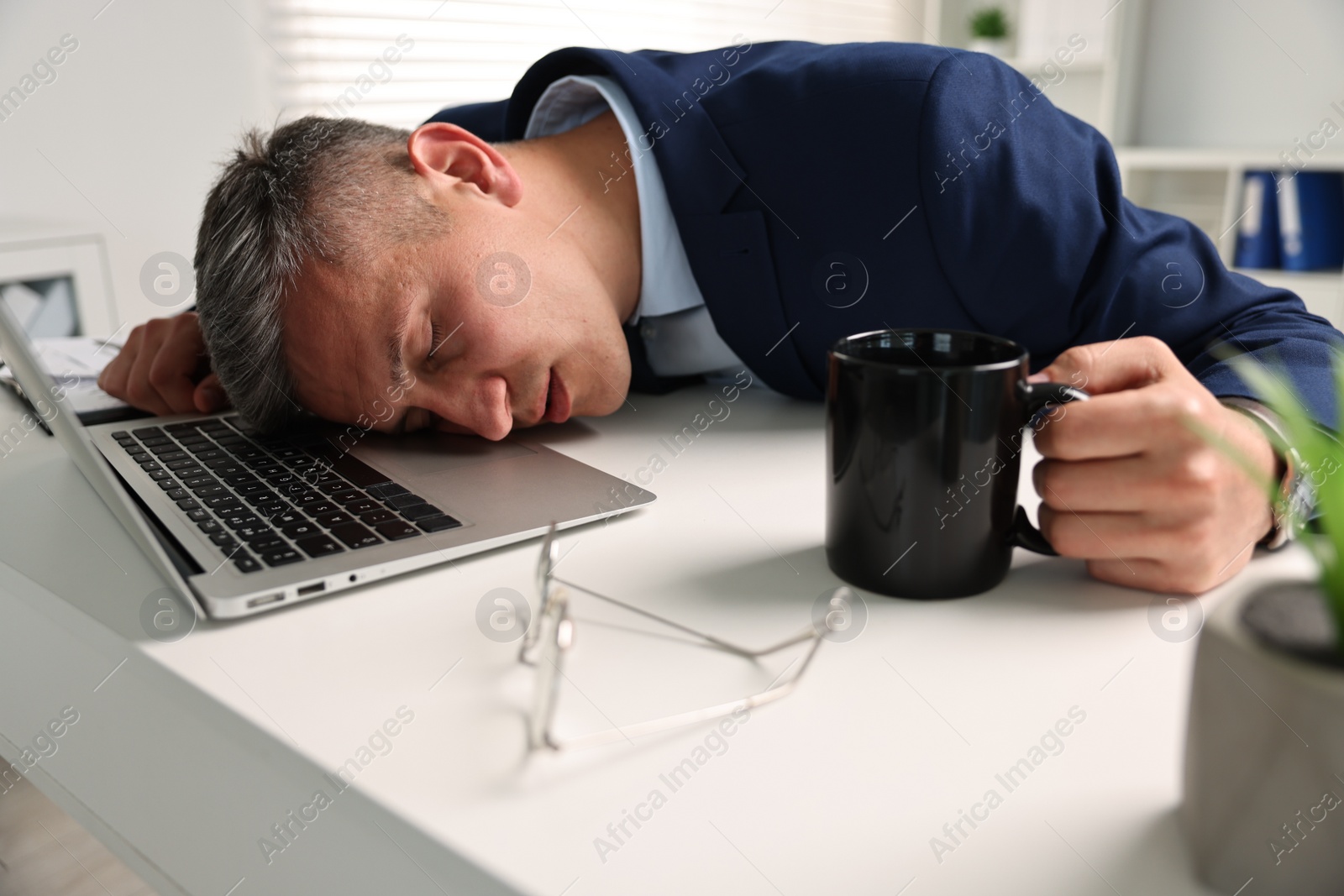 Photo of Man with cup of drink sleeping at table in office