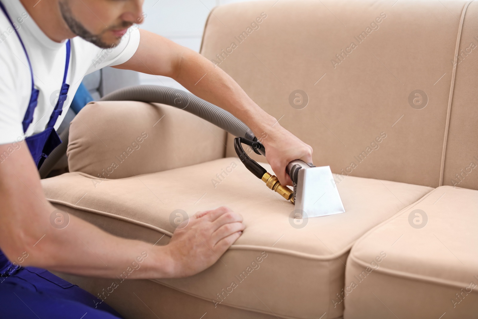 Photo of Dry cleaning worker removing dirt from sofa indoors