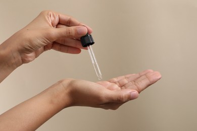 Woman applying cosmetic serum onto her hand on beige background, closeup. Space for text