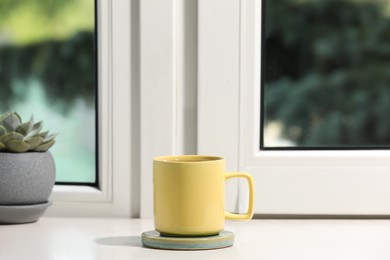 Yellow cup of tea and succulent on white window sill