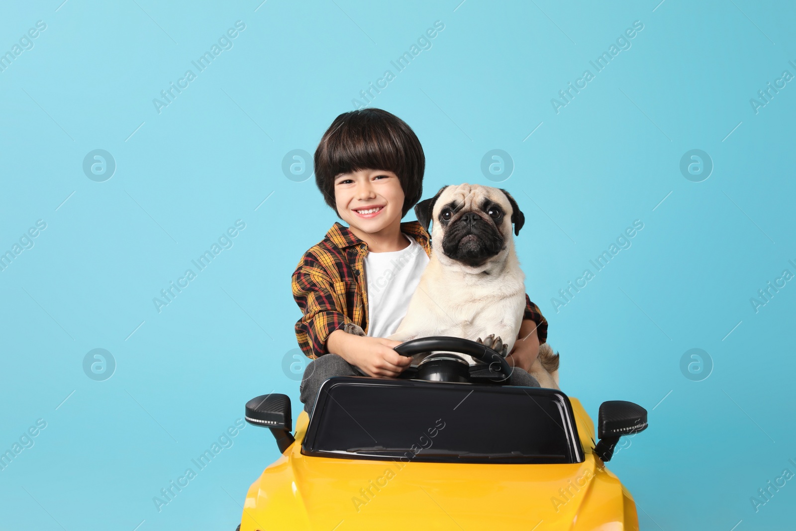 Photo of Little boy with his dog in toy car on light blue background