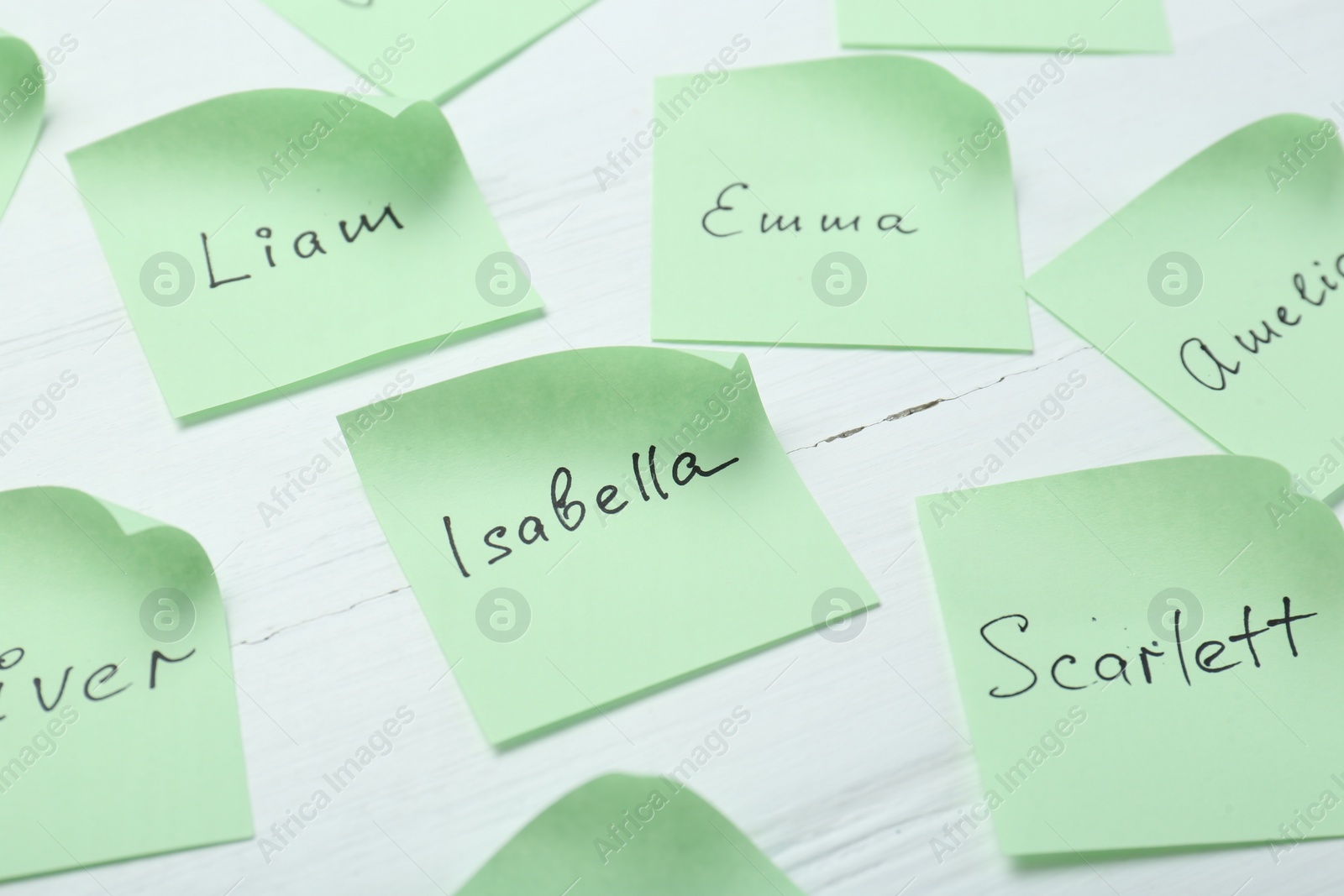 Photo of Paper stickers with different names on white wooden table, closeup. Choosing baby's name