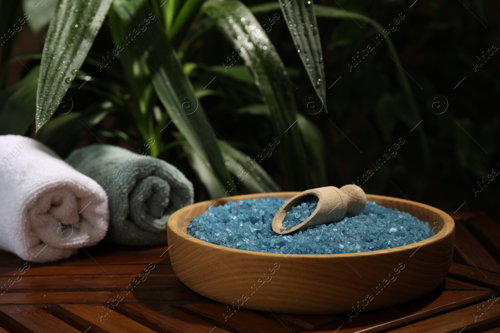 Photo of Bowl of blue sea salt with scoop and rolled towels on wooden table