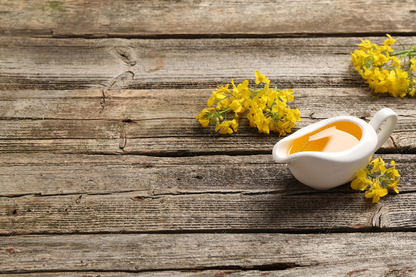 Photo of Rapeseed oil in gravy boat and beautiful yellow flowers on wooden table, space for text