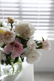 Beautiful peonies in vase on table near window indoors