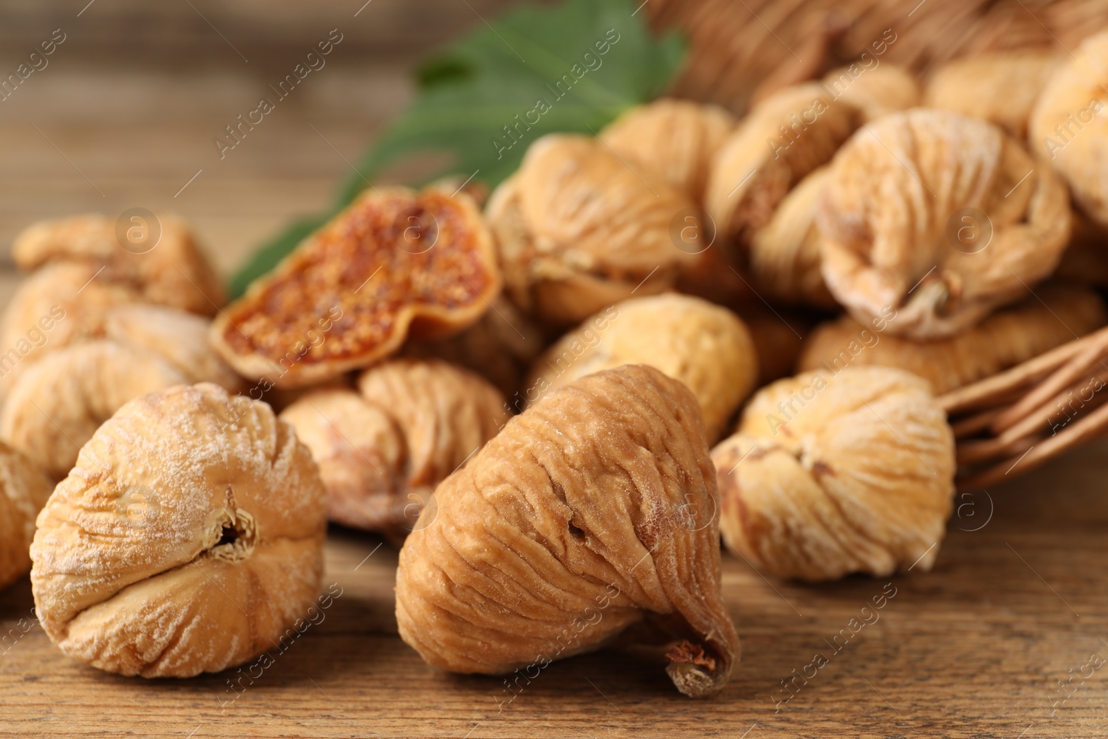 Photo of Overturned wicker basket and dried figs on wooden table, closeup