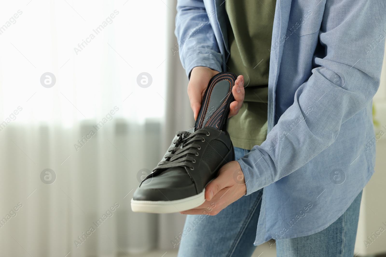 Photo of Man putting orthopedic insole into shoe indoors, closeup. Space for text