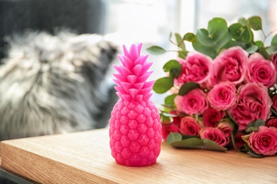 Pineapple shaped candle and bouquet of flowers on table in room